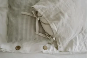 Bantal dan cadar linen warna krim dengan butang kayu dalam cahaya lembut
