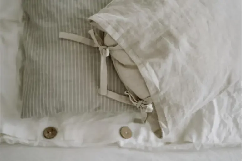Bantal dan cadar linen warna krim dengan butang kayu dalam cahaya lembut