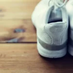 Sepasang kasut sukan putih diletak di atas lantai kayu