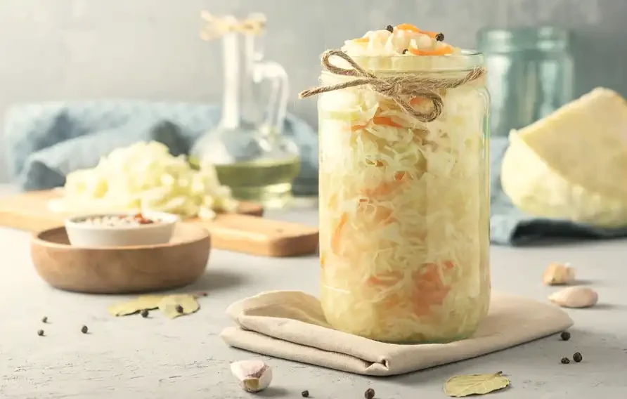 Balang kaca berisi kubis jeruk dengan bawang putih dan daun bay di atas meja