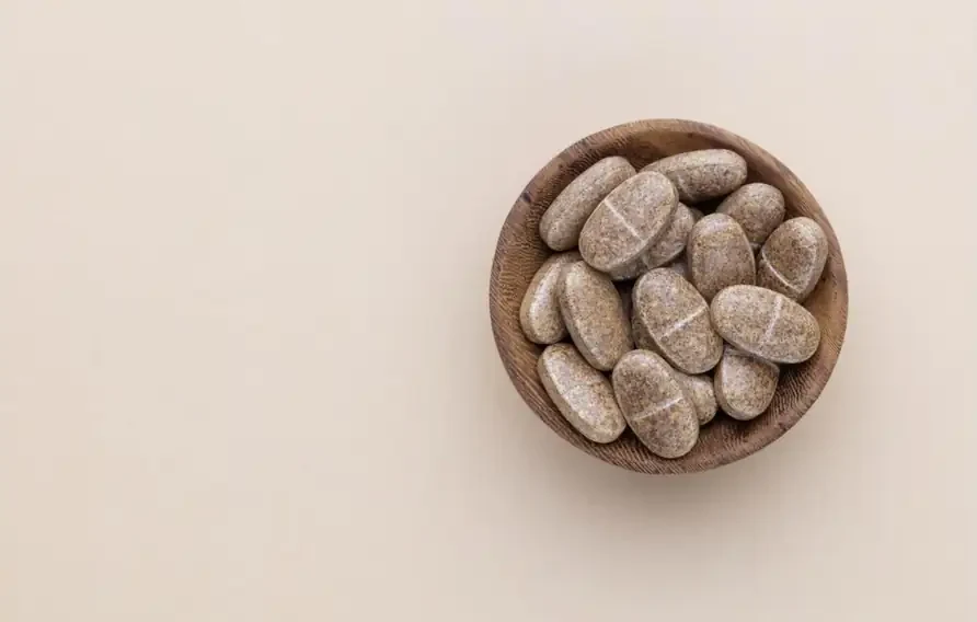 Tablet suplemen dalam mangkuk kayu di atas latar warna krim